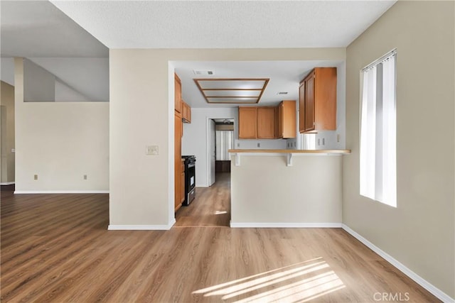 kitchen with electric stove, kitchen peninsula, a breakfast bar area, and light hardwood / wood-style flooring