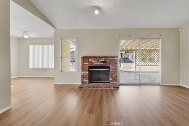 unfurnished living room featuring hardwood / wood-style flooring, ceiling fan, a brick fireplace, and a textured ceiling