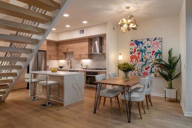 kitchen featuring wall chimney range hood, hanging light fixtures, stainless steel appliances, tasteful backsplash, and a kitchen island