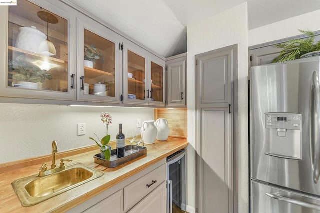 kitchen with lofted ceiling, butcher block counters, sink, stainless steel fridge, and beverage cooler