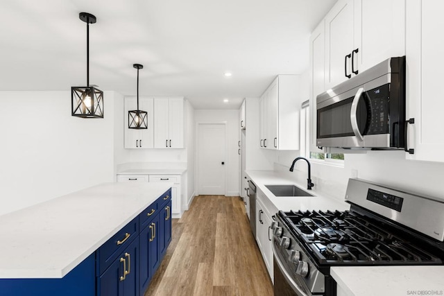 kitchen featuring appliances with stainless steel finishes, decorative light fixtures, white cabinetry, sink, and blue cabinetry