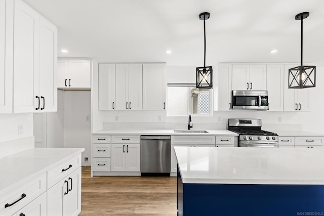 kitchen featuring sink, white cabinetry, light hardwood / wood-style flooring, pendant lighting, and stainless steel appliances