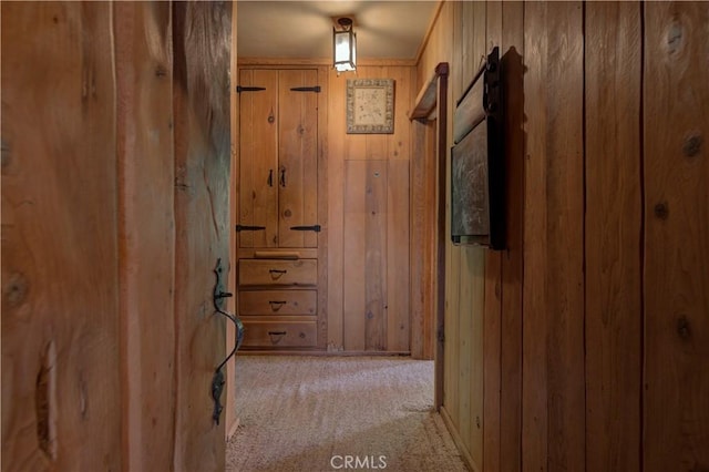 hallway featuring light colored carpet and wood walls