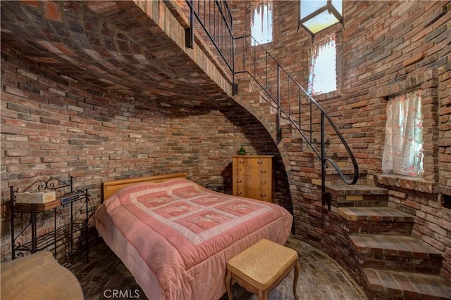 unfurnished bedroom with a high ceiling, brick wall, and hardwood / wood-style flooring