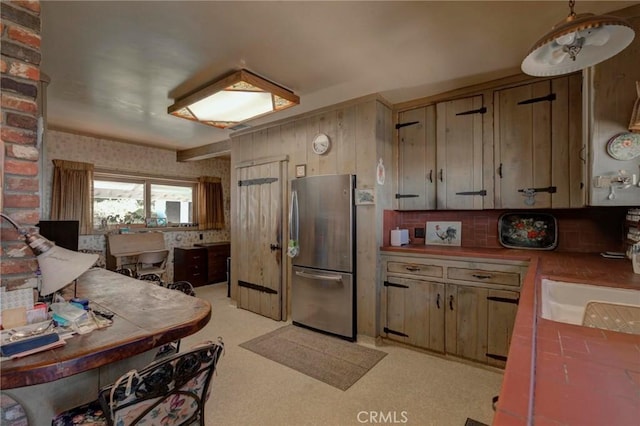 kitchen with sink, stainless steel refrigerator, backsplash, tile counters, and decorative light fixtures