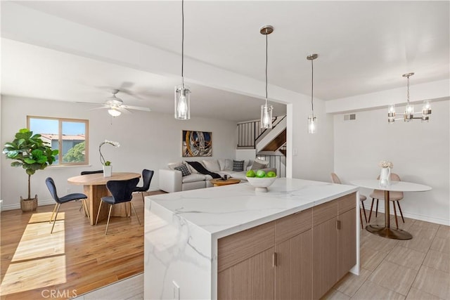 kitchen with decorative light fixtures, a center island, ceiling fan, light stone countertops, and light wood-type flooring