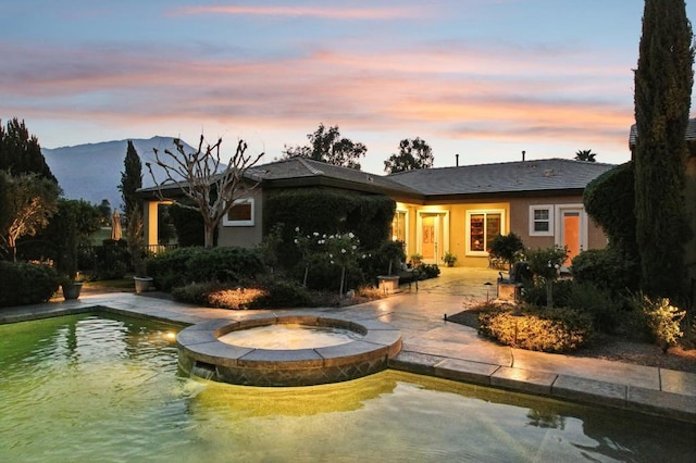 back house at dusk featuring a swimming pool with hot tub, a mountain view, and a patio