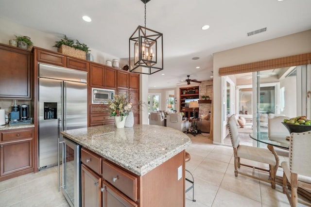 kitchen featuring light stone counters, built in appliances, a center island, pendant lighting, and beverage cooler