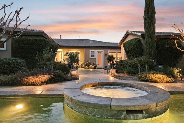 back house at dusk featuring an in ground hot tub