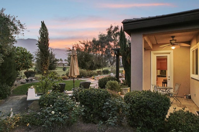 yard at dusk with ceiling fan and a patio area