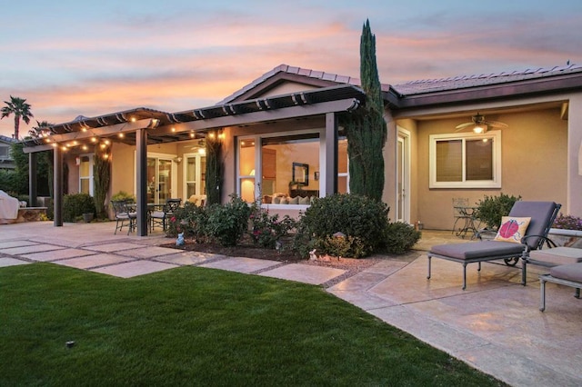 back house at dusk with a patio, ceiling fan, and a lawn