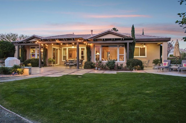 back house at dusk featuring a patio area and a lawn