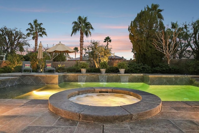 patio terrace at dusk featuring an in ground hot tub and pool water feature