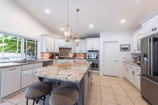 kitchen with appliances with stainless steel finishes, decorative light fixtures, white cabinetry, sink, and a center island