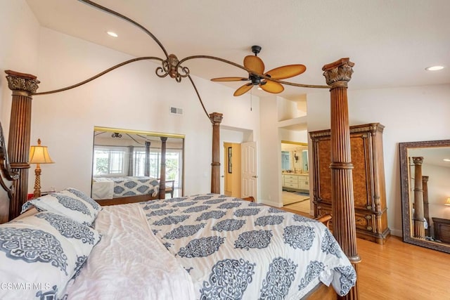 bedroom with ornate columns, ensuite bathroom, high vaulted ceiling, and light wood-type flooring