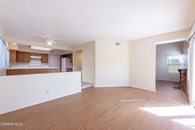 unfurnished living room with ceiling fan, sink, and light wood-type flooring