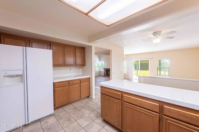 kitchen with light tile patterned floors, tile countertops, white fridge with ice dispenser, and ceiling fan