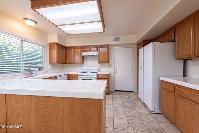 kitchen with sink, white appliances, light tile patterned floors, tile counters, and kitchen peninsula