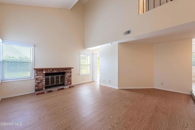 unfurnished living room with a brick fireplace, plenty of natural light, a high ceiling, and light wood-type flooring