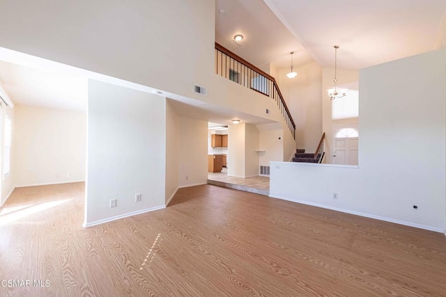 unfurnished living room featuring a notable chandelier, light hardwood / wood-style floors, and high vaulted ceiling