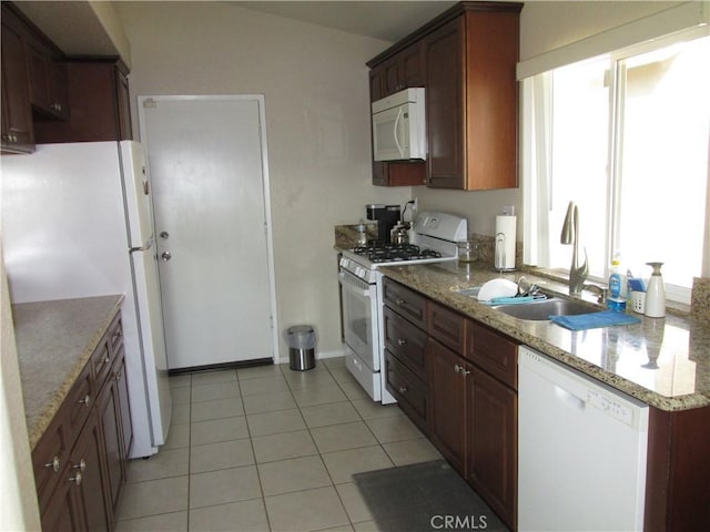 kitchen with light tile patterned flooring, white appliances, light stone countertops, and sink