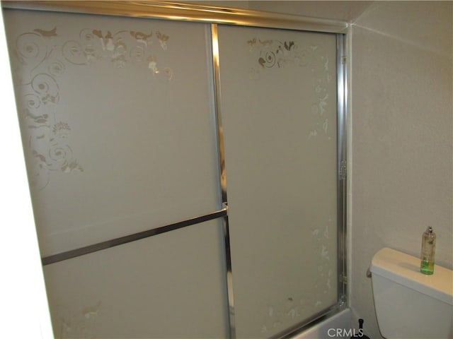 bathroom featuring combined bath / shower with glass door and toilet