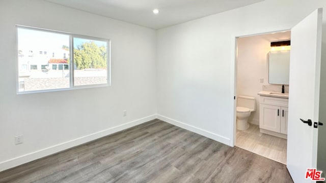 unfurnished bedroom featuring sink, hardwood / wood-style floors, and ensuite bath