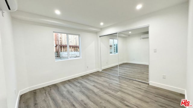 unfurnished bedroom with hardwood / wood-style floors, a wall mounted air conditioner, and a closet