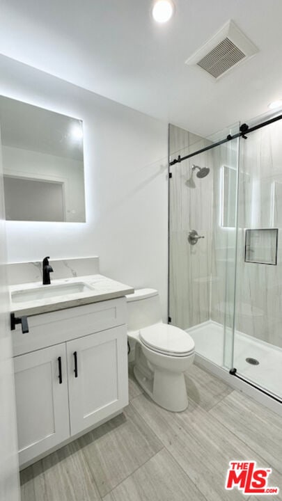 bathroom featuring vanity, toilet, and a shower with shower door