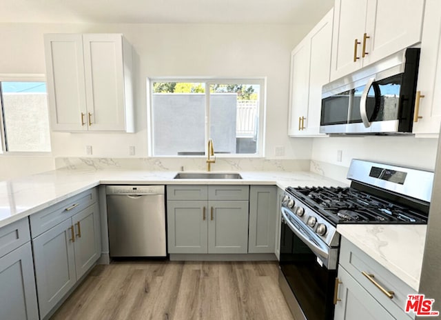 kitchen featuring sink, appliances with stainless steel finishes, gray cabinetry, light stone countertops, and light hardwood / wood-style floors