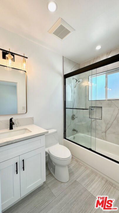 full bathroom featuring vanity, shower / bath combination with glass door, and toilet