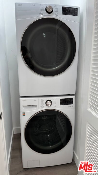 clothes washing area with stacked washer and dryer and dark wood-type flooring