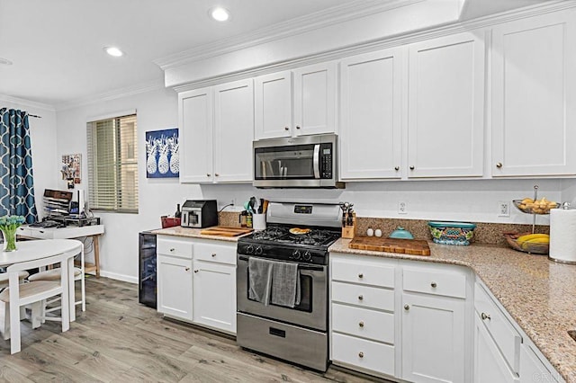 kitchen with stainless steel appliances, white cabinetry, light stone counters, and crown molding