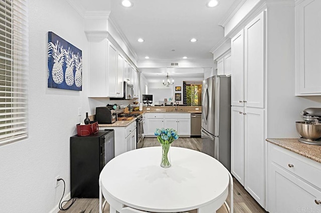 kitchen featuring stainless steel appliances, hanging light fixtures, white cabinets, and light hardwood / wood-style flooring