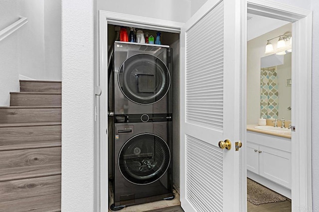 laundry room with stacked washing maching and dryer, wood-type flooring, and sink