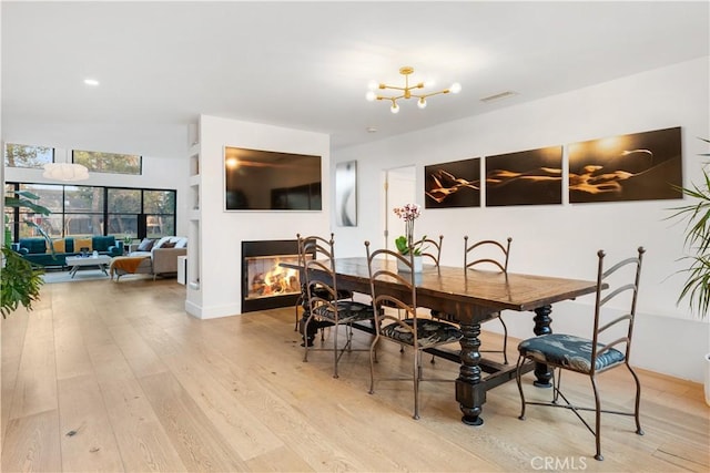 dining room featuring an inviting chandelier, light hardwood / wood-style floors, and a multi sided fireplace