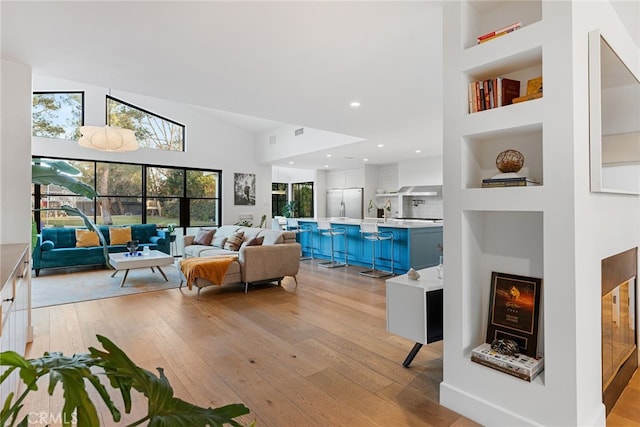 living room with built in features, light hardwood / wood-style flooring, and high vaulted ceiling