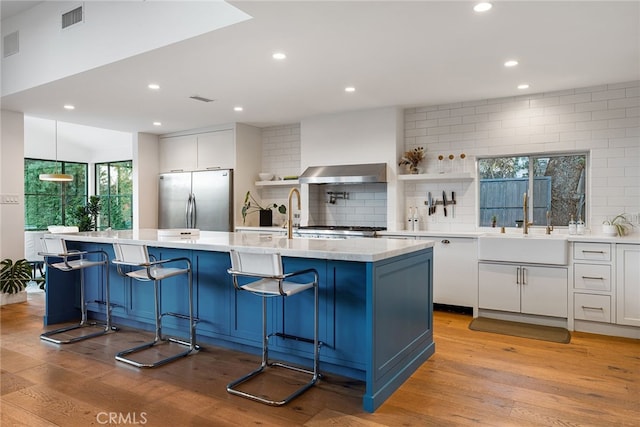 kitchen featuring stainless steel refrigerator, white cabinetry, a kitchen breakfast bar, and a center island with sink