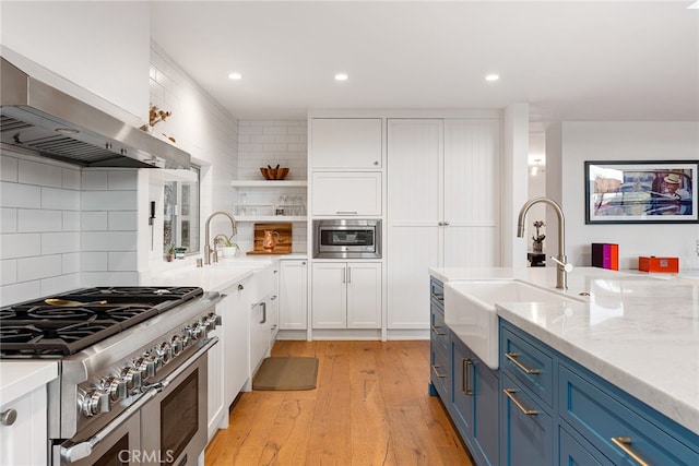 kitchen featuring white cabinetry, blue cabinets, wall chimney exhaust hood, and range with two ovens