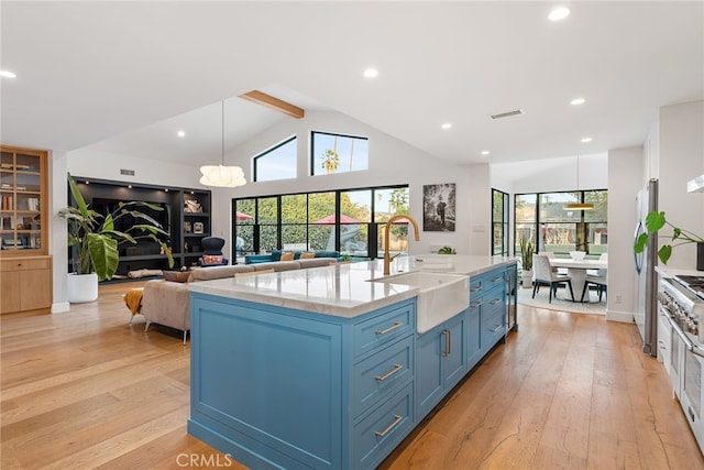 kitchen featuring blue cabinetry, sink, a center island with sink, light wood-type flooring, and pendant lighting