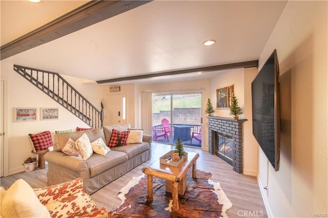 living room with beamed ceiling, a brick fireplace, and light wood-type flooring