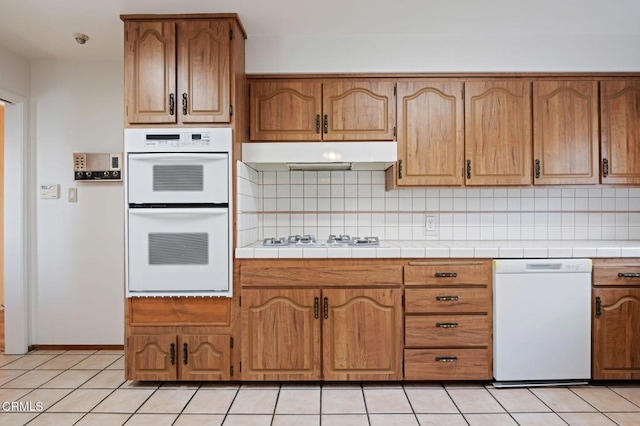 kitchen featuring backsplash, white appliances, tile counters, and light tile patterned floors