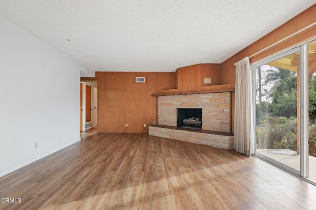 unfurnished living room featuring a stone fireplace, light hardwood / wood-style floors, a textured ceiling, and wood walls