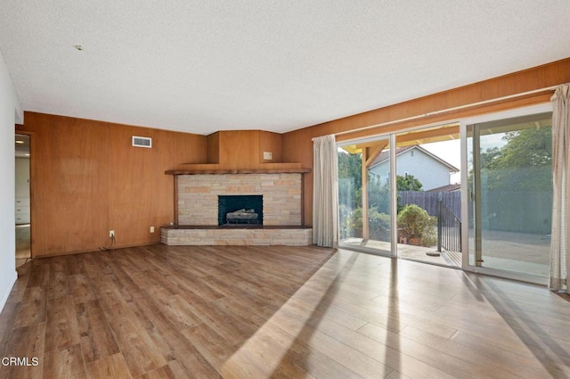 unfurnished living room featuring a stone fireplace, light hardwood / wood-style floors, a textured ceiling, and wood walls