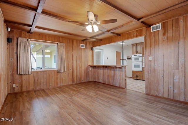 unfurnished living room with beam ceiling, wooden walls, and light wood-type flooring