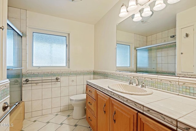 bathroom with tile patterned flooring, tile walls, vanity, a shower with shower door, and toilet