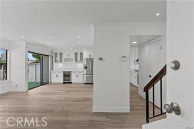 unfurnished living room featuring wine cooler, crown molding, and light hardwood / wood-style floors