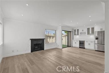 unfurnished living room featuring bar, beverage cooler, and light hardwood / wood-style floors