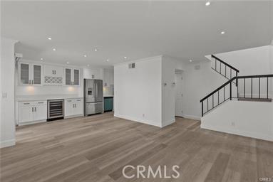 unfurnished living room with bar area, beverage cooler, and light wood-type flooring