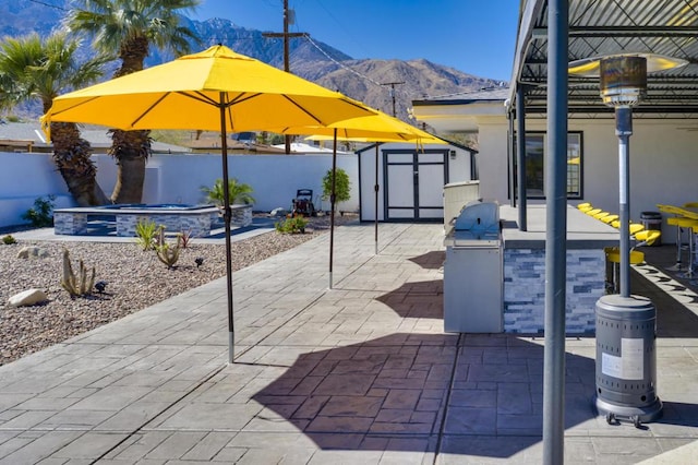 view of patio / terrace featuring exterior kitchen, an in ground hot tub, a mountain view, and a storage unit